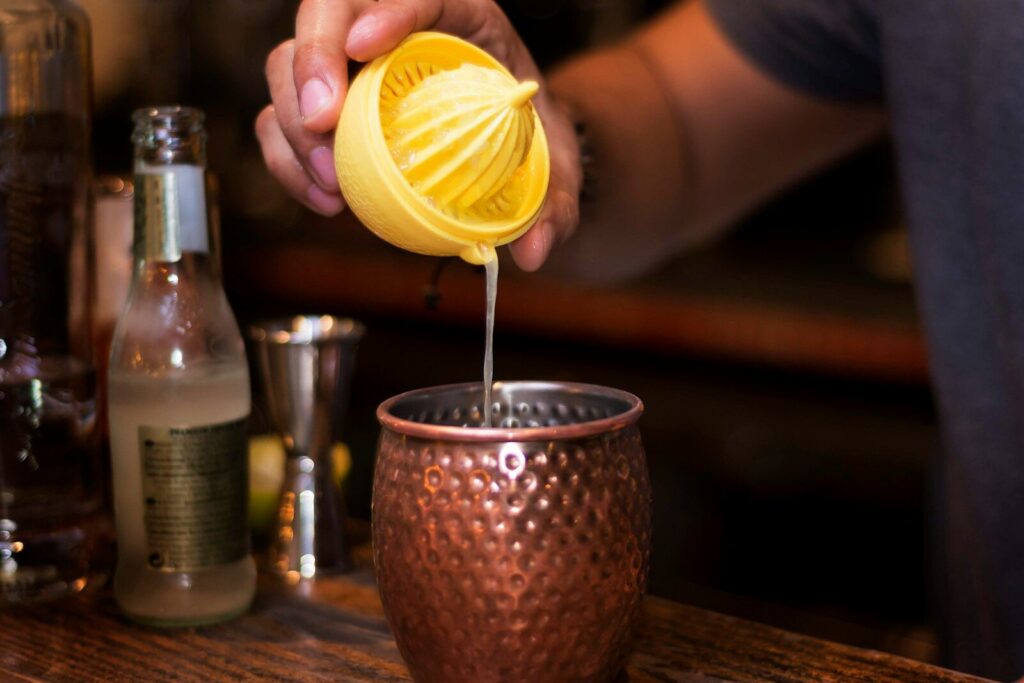 person pouring yellow lemon on clear drinking glass