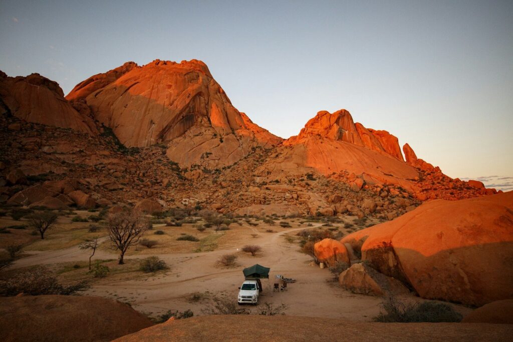 Camper van parked in a desert valley with red mountains.